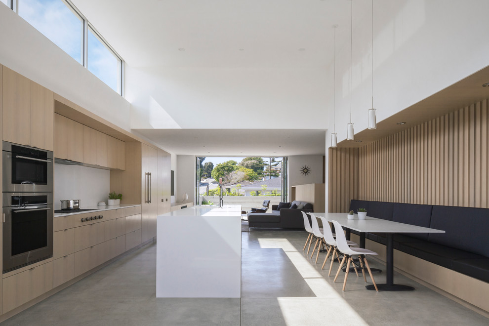На фото: параллельная кухня-гостиная в стиле модернизм с врезной мойкой, плоскими фасадами, светлыми деревянными фасадами, белым фартуком, фартуком из стеклянной плитки, техникой под мебельный фасад, бетонным полом, островом и серым полом