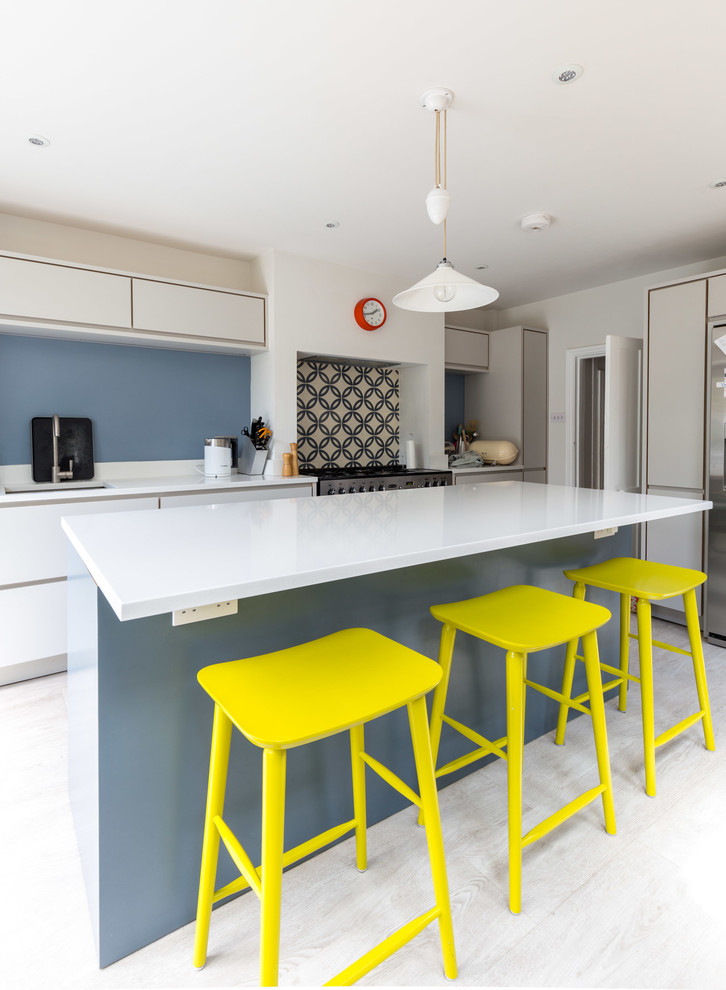 This is an example of a contemporary galley kitchen in Sussex with flat-panel cabinets, white cabinets, stainless steel appliances, light hardwood flooring and an island.