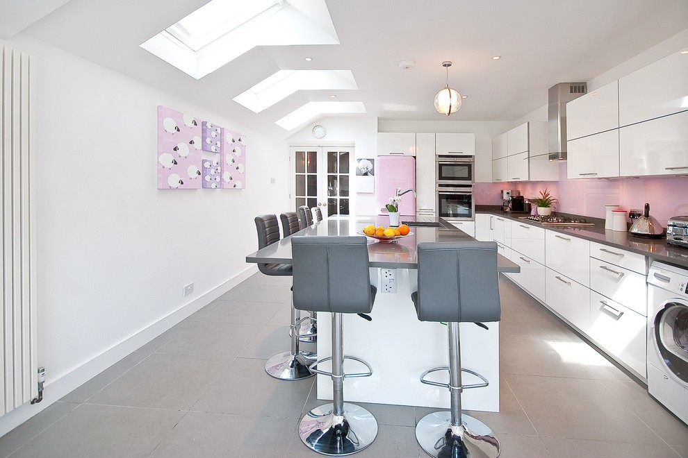 Moderne Küche in L-Form mit Unterbauwaschbecken, flächenbündigen Schrankfronten, weißen Schränken, Küchenrückwand in Rosa, Glasrückwand, bunten Elektrogeräten und Kücheninsel in Surrey