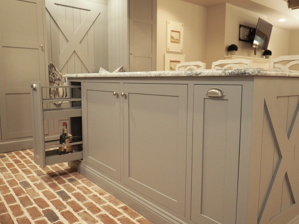 Inspiration for a medium sized farmhouse l-shaped kitchen/diner in Atlanta with a belfast sink, grey cabinets, granite worktops, stainless steel appliances, brick flooring, an island, red floors, grey worktops, shaker cabinets, white splashback and wood splashback.
