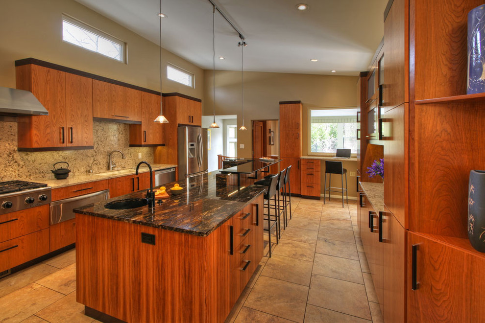 Cette photo montre une cuisine américaine moderne en U et bois clair avec un évier encastré, un placard à porte plane, un plan de travail en granite et un électroménager en acier inoxydable.