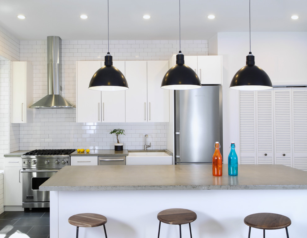 Eat-in kitchen - mid-sized modern l-shaped slate floor eat-in kitchen idea in New York with a farmhouse sink, flat-panel cabinets, white cabinets, concrete countertops, white backsplash, subway tile backsplash, stainless steel appliances and an island