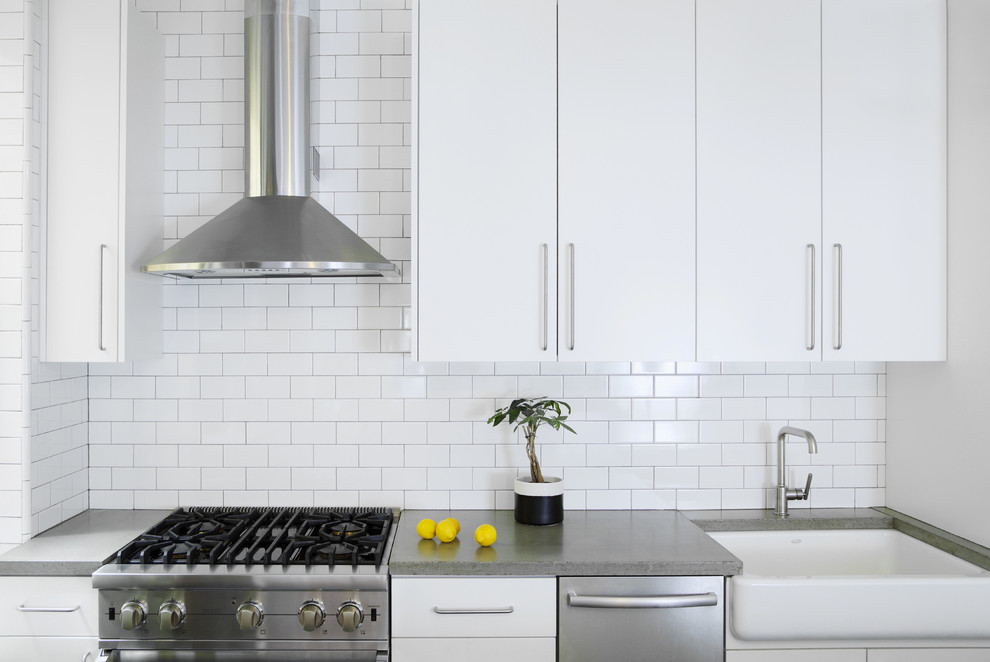 Inspiration for a medium sized modern l-shaped kitchen/diner in New York with a belfast sink, flat-panel cabinets, white cabinets, concrete worktops, white splashback, metro tiled splashback, stainless steel appliances, slate flooring and an island.