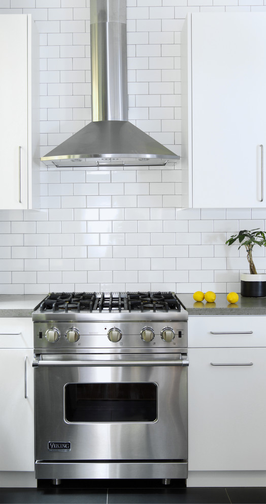 Example of a mid-sized minimalist l-shaped slate floor eat-in kitchen design in New York with a farmhouse sink, flat-panel cabinets, white cabinets, concrete countertops, white backsplash, subway tile backsplash, stainless steel appliances and an island