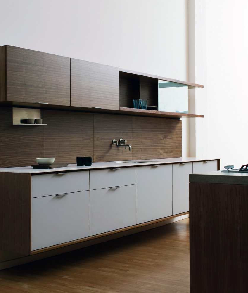 Example of a minimalist galley kitchen design in New York with solid surface countertops, an undermount sink, flat-panel cabinets, white cabinets and brown backsplash