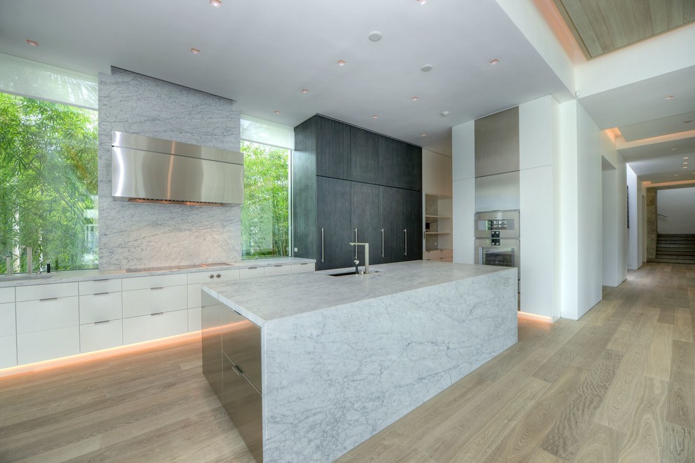 Modern inredning av ett mycket stort kök, med en undermonterad diskho, släta luckor, vita skåp, marmorbänkskiva, vitt stänkskydd, stänkskydd i sten, rostfria vitvaror, ljust trägolv och en köksö