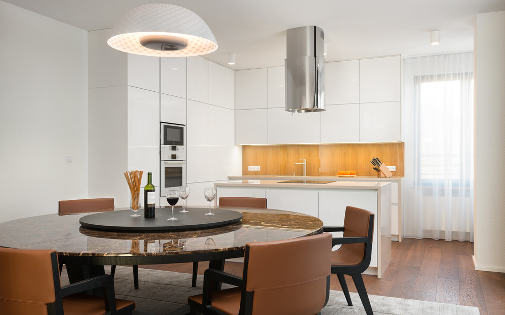 Mittelgroße Moderne Wohnküche in L-Form mit flächenbündigen Schrankfronten, weißen Schränken, Glasrückwand, weißen Elektrogeräten, dunklem Holzboden und Kücheninsel in Sonstige