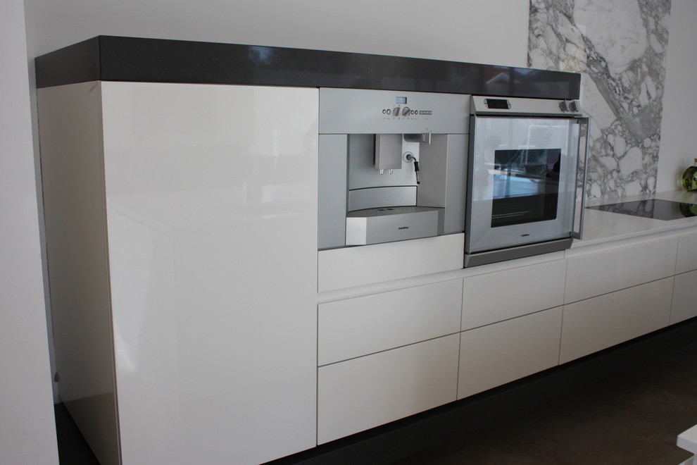 Large minimalist single-wall black floor open concept kitchen photo in Melbourne with flat-panel cabinets, white cabinets, solid surface countertops, gray backsplash, marble backsplash, stainless steel appliances and an island