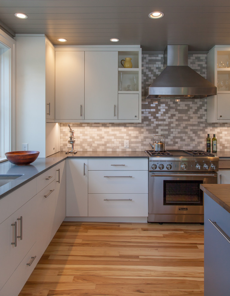 Example of a large trendy l-shaped light wood floor eat-in kitchen design in Burlington with flat-panel cabinets, white cabinets, wood countertops, gray backsplash, stainless steel appliances, an island, an undermount sink and porcelain backsplash