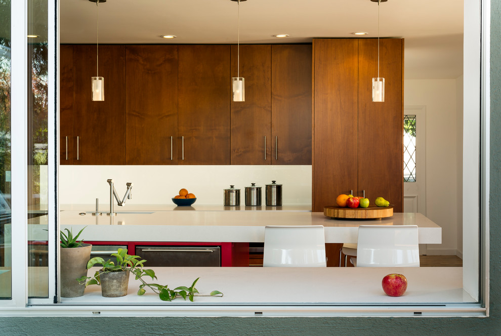 This is an example of a medium sized contemporary u-shaped kitchen in San Francisco with flat-panel cabinets, medium wood cabinets, engineered stone countertops, white splashback, an island, a submerged sink, glass sheet splashback, stainless steel appliances and porcelain flooring.