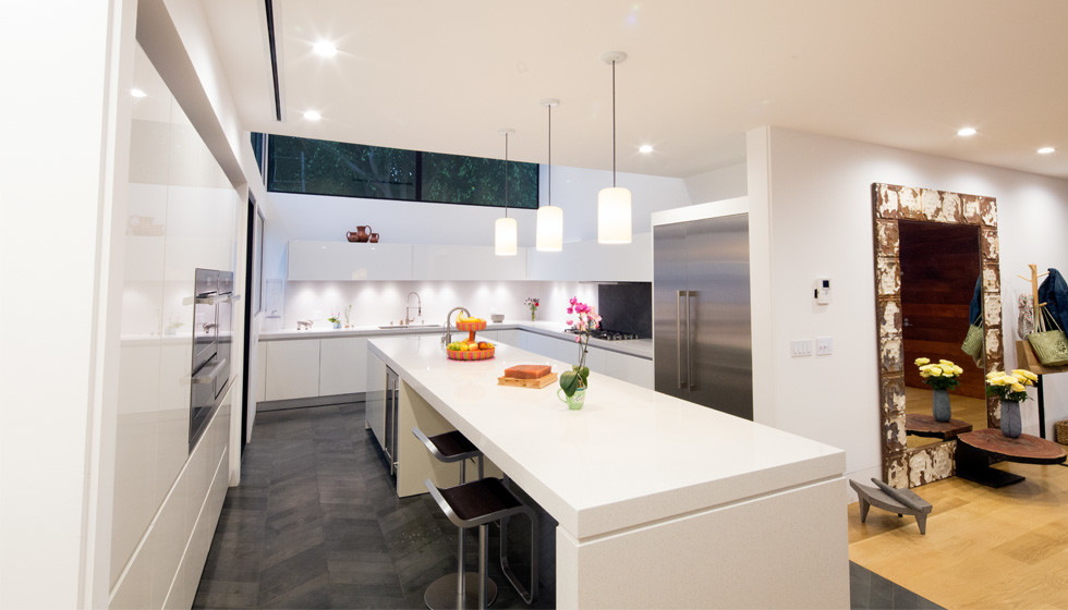 Inspiration for a large modern u-shaped painted wood floor eat-in kitchen remodel in Los Angeles with an undermount sink, flat-panel cabinets, white cabinets, solid surface countertops, white backsplash, stone tile backsplash, stainless steel appliances and an island