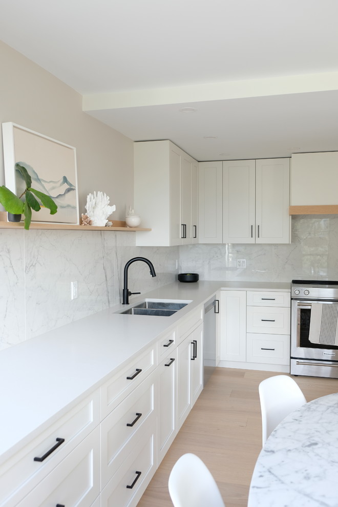 Photo of a scandi kitchen in Vancouver with engineered stone countertops, white splashback, porcelain splashback, stainless steel appliances, light hardwood flooring and white worktops.