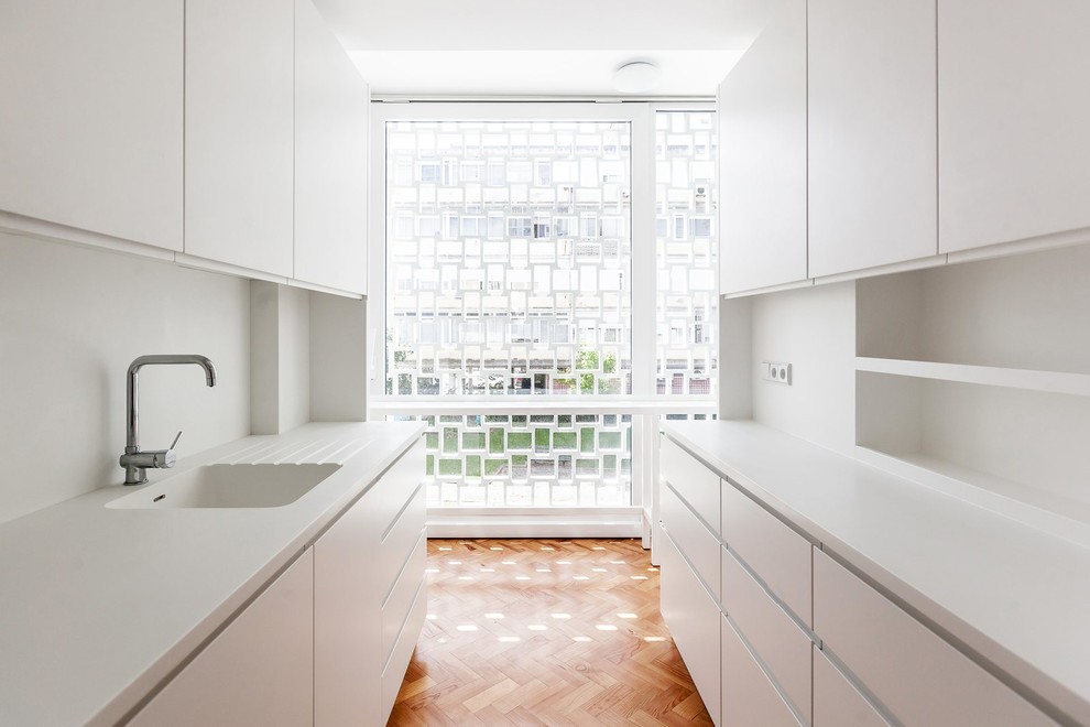 This is an example of a medium sized modern galley enclosed kitchen in Other with an integrated sink, flat-panel cabinets, white cabinets, white splashback, medium hardwood flooring and no island.