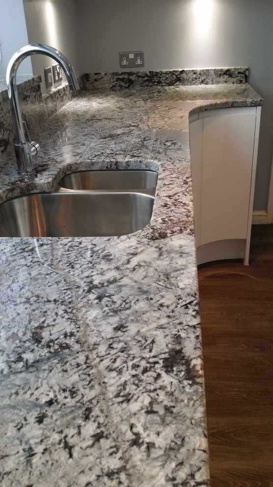 Foto på ett avskilt, mellanstort funkis u-kök, med en integrerad diskho, släta luckor, vita skåp, granitbänkskiva, flerfärgad stänkskydd, stänkskydd i sten, integrerade vitvaror och vinylgolv