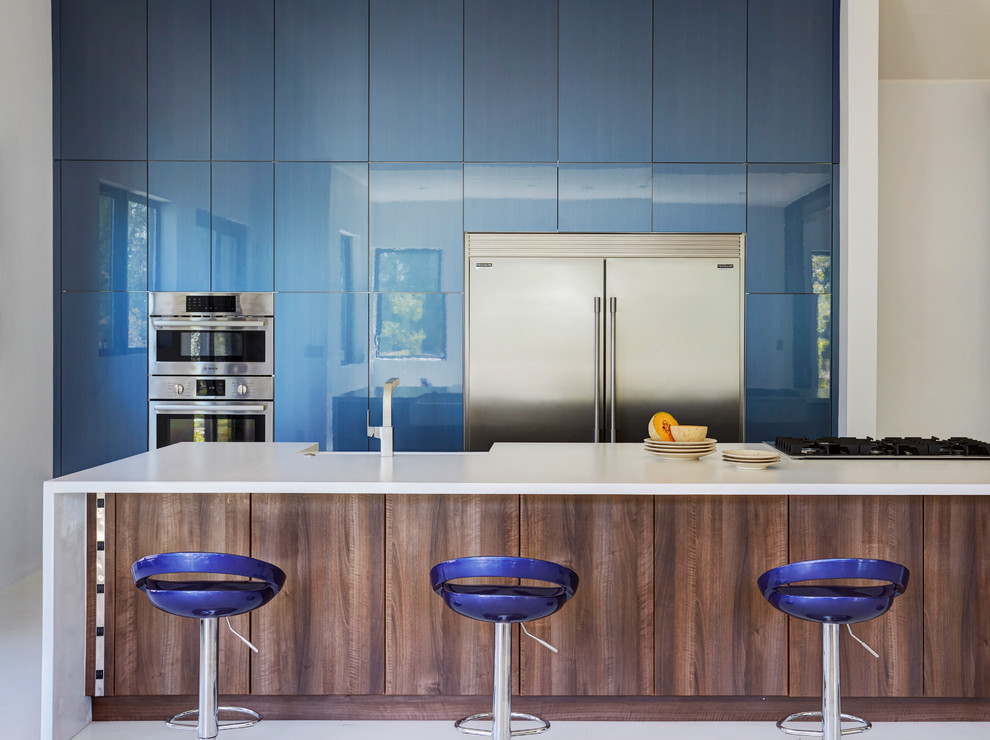 Cette photo montre une cuisine tendance avec un placard à porte plane, des portes de placard bleues, un électroménager en acier inoxydable, îlot, un sol blanc et un plan de travail blanc.