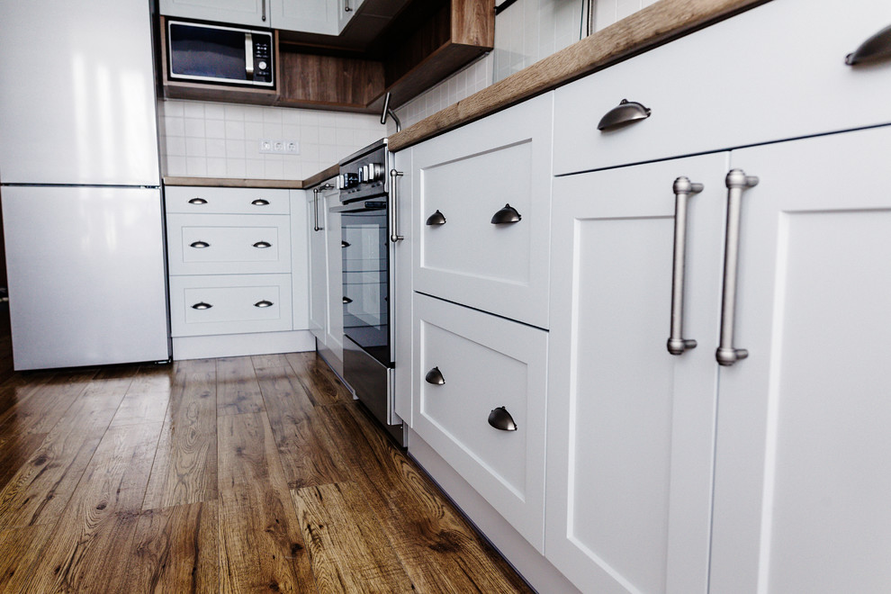 Photo of a medium sized traditional u-shaped kitchen/diner in DC Metro with a built-in sink, recessed-panel cabinets, white cabinets, wood worktops, white splashback, ceramic splashback, stainless steel appliances, dark hardwood flooring, a breakfast bar, brown floors and brown worktops.