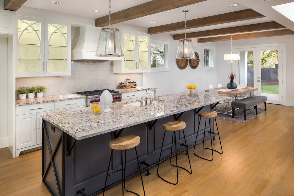 Example of a large farmhouse l-shaped light wood floor and beige floor open concept kitchen design in DC Metro with an undermount sink, raised-panel cabinets, white cabinets, granite countertops, gray backsplash, ceramic backsplash, stainless steel appliances, an island and multicolored countertops
