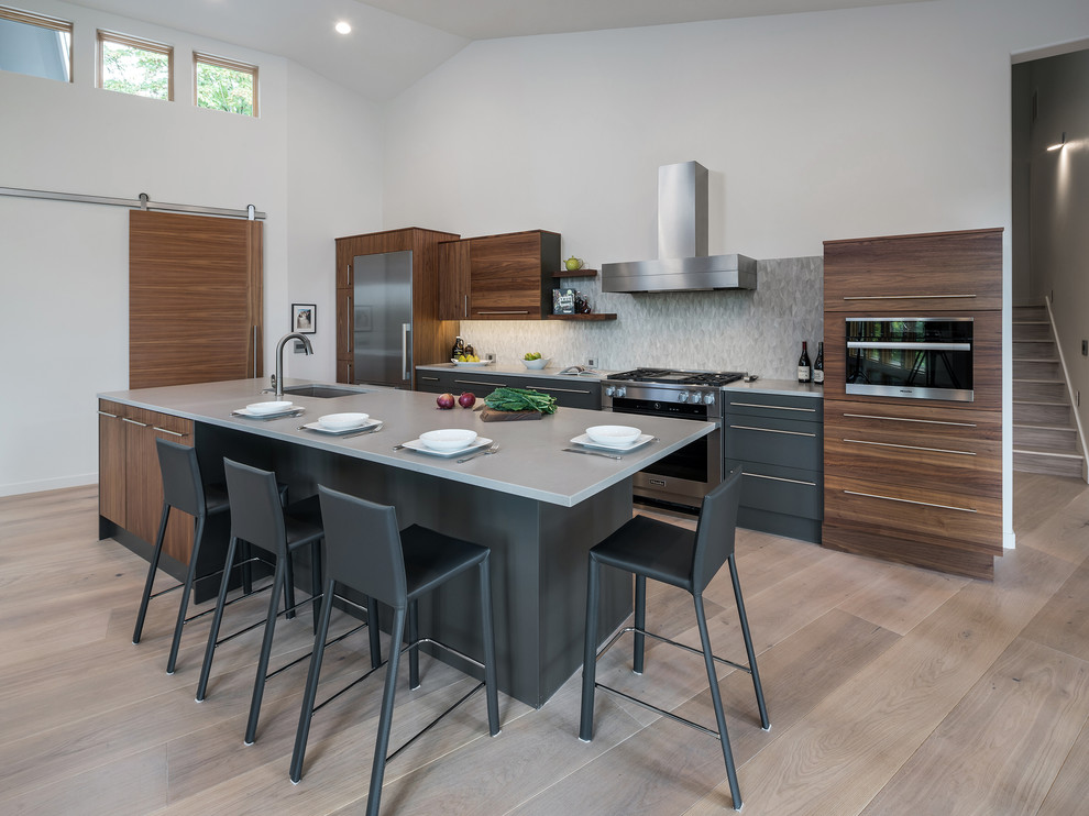 Photo of a modern galley kitchen in Portland with flat-panel cabinets, dark wood cabinets, grey splashback, stainless steel appliances, light hardwood flooring, an island and brown floors.