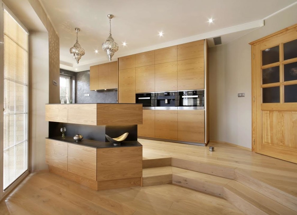 Cette image montre une grande cuisine parallèle design en bois clair avec un placard à porte plane, un électroménager en acier inoxydable, parquet clair, une péninsule et un sol beige.