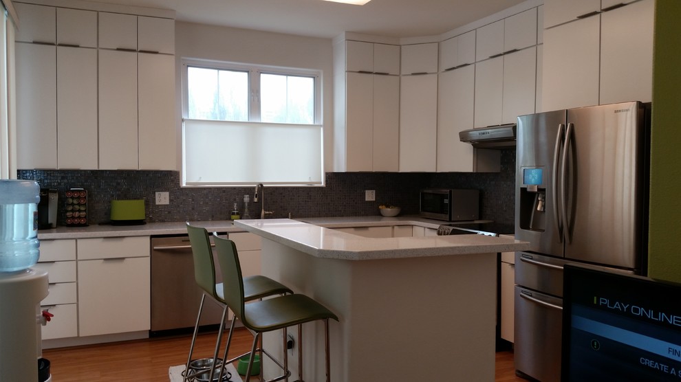 This is an example of a mid-sized modern l-shaped eat-in kitchen in Kansas City with with island, glass-front cabinets, white cabinets, recycled glass benchtops, metallic splashback, glass tile splashback, stainless steel appliances, an undermount sink and medium hardwood floors.