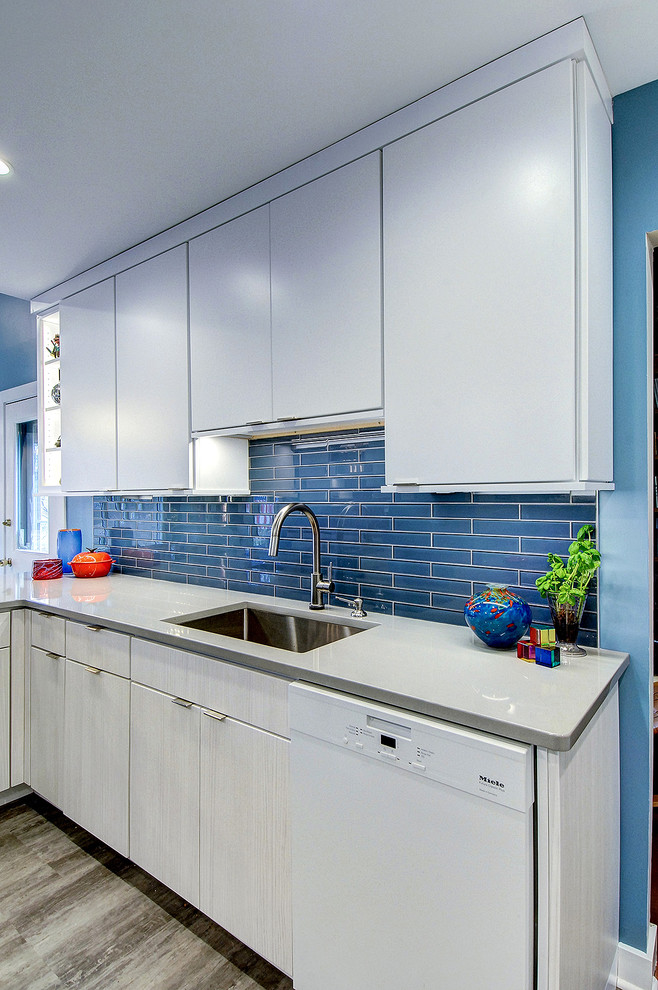 フィラデルフィアにある高級な中くらいなモダンスタイルのおしゃれなキッチン (アンダーカウンターシンク、フラットパネル扉のキャビネット、白いキャビネット、珪岩カウンター、青いキッチンパネル、ガラスタイルのキッチンパネル、パネルと同色の調理設備、クッションフロア、グレーの床、グレーのキッチンカウンター) の写真