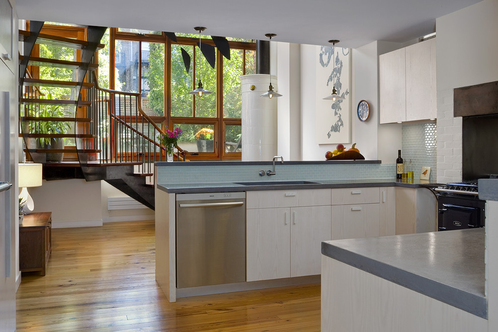 Modelo de cocina minimalista con salpicadero de azulejos de vidrio, fregadero bajoencimera, encimera de cemento, electrodomésticos negros, armarios con paneles lisos y salpicadero azul