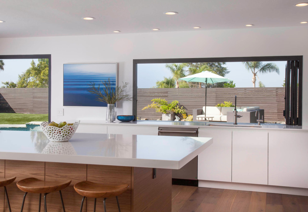 Design ideas for a large modern l-shaped open plan kitchen in San Diego with a submerged sink, flat-panel cabinets, white cabinets, engineered stone countertops, white splashback, glass tiled splashback, stainless steel appliances, medium hardwood flooring, an island, beige floors and white worktops.