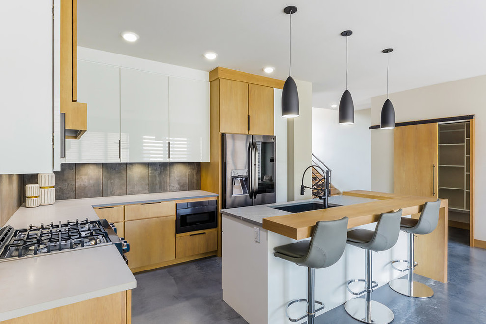 Inredning av ett modernt mellanstort kök, med en undermonterad diskho, släta luckor, vita skåp, granitbänkskiva, svart stänkskydd, stänkskydd i keramik, svarta vitvaror, betonggolv, en köksö och grått golv