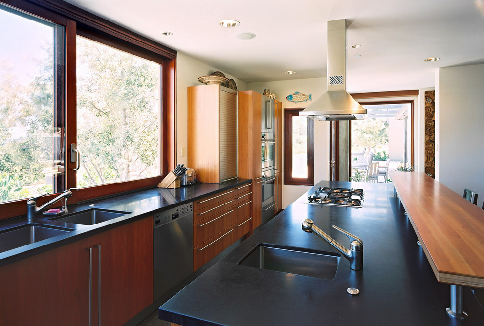 Inredning av ett modernt kök, med granitbänkskiva, rostfria vitvaror, en undermonterad diskho, släta luckor och skåp i mellenmörkt trä