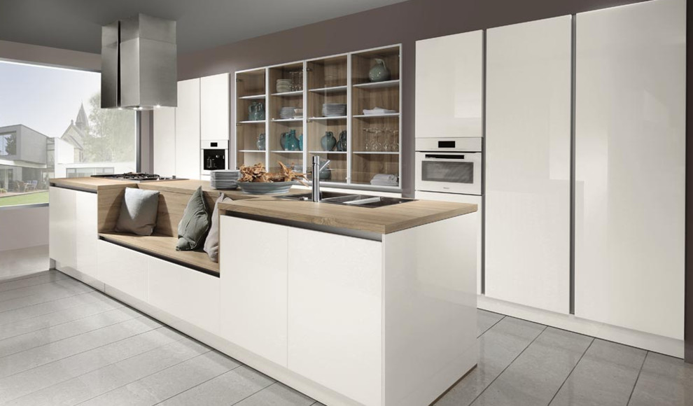Photo of a large modern galley kitchen/diner in Toronto with a triple-bowl sink, flat-panel cabinets, white cabinets, wood worktops, porcelain flooring, an island and integrated appliances.