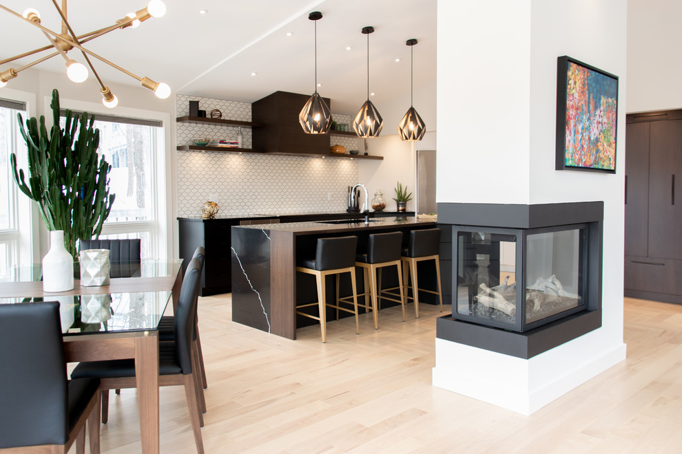 Modern inredning av ett stort svart svart kök, med bänkskiva i kvartsit, rostfria vitvaror, ljust trägolv, en köksö, beiget golv, en undermonterad diskho, släta luckor, svarta skåp, vitt stänkskydd och stänkskydd i mosaik