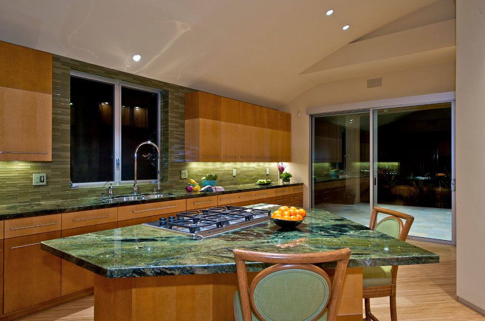 Moderne Küche mit Doppelwaschbecken, flächenbündigen Schrankfronten, hellen Holzschränken, Küchenrückwand in Grün, Rückwand aus Glasfliesen, Küchengeräten aus Edelstahl, Granit-Arbeitsplatte, hellem Holzboden, Kücheninsel und grüner Arbeitsplatte in San Diego