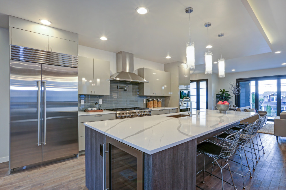 Eat-in kitchen - large modern galley bamboo floor and brown floor eat-in kitchen idea in San Francisco with a drop-in sink, flat-panel cabinets, white cabinets, quartz countertops, blue backsplash, glass sheet backsplash, stainless steel appliances, an island and gray countertops