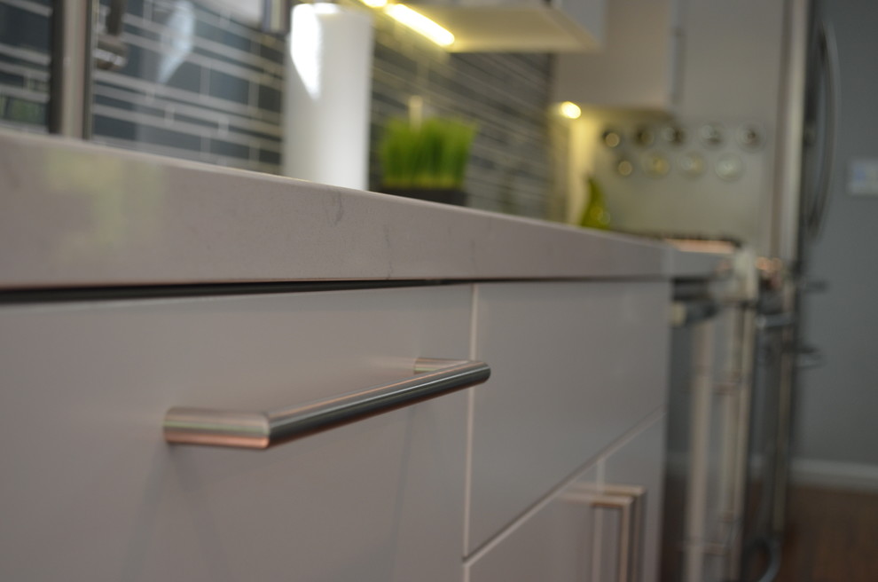 Modern inredning av ett mellanstort kök, med en undermonterad diskho, släta luckor, blå skåp, bänkskiva i kvartsit, grått stänkskydd, stänkskydd i glaskakel, rostfria vitvaror, mellanmörkt trägolv och en köksö