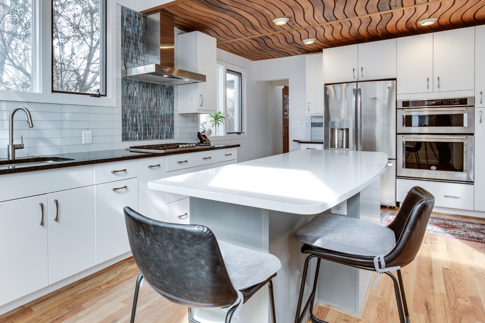 Bild på ett mellanstort funkis kök, med en undermonterad diskho, släta luckor, bänkskiva i kvarts, vitt stänkskydd, stänkskydd i glaskakel, rostfria vitvaror, mellanmörkt trägolv och en köksö