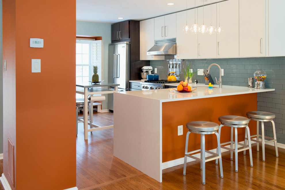 Mid-sized trendy galley medium tone wood floor eat-in kitchen photo in DC Metro with flat-panel cabinets, white cabinets, blue backsplash, an undermount sink, ceramic backsplash, stainless steel appliances and an island