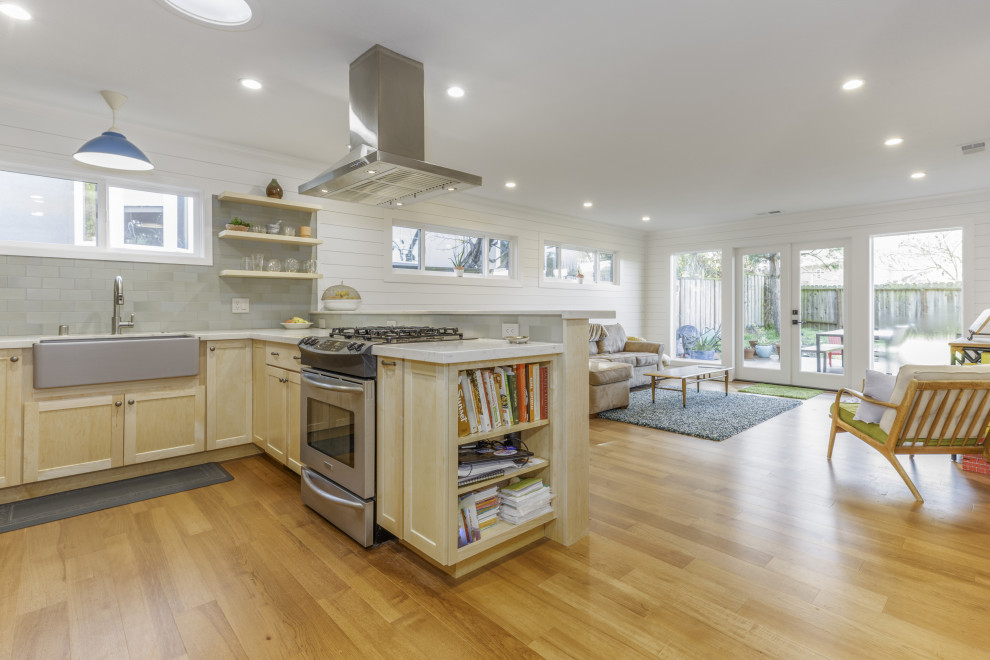 This is an example of a medium sized coastal u-shaped open plan kitchen in San Francisco with a belfast sink, open cabinets, light wood cabinets, marble worktops, green splashback, ceramic splashback, stainless steel appliances, light hardwood flooring, a breakfast bar, brown floors and white worktops.