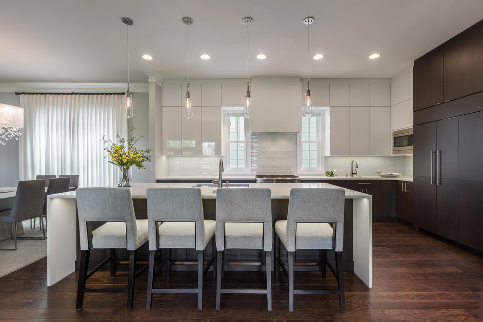 Ejemplo de cocina contemporánea con fregadero bajoencimera, armarios con paneles lisos, puertas de armario de madera en tonos medios, salpicadero blanco, electrodomésticos de acero inoxidable, suelo de madera oscura, una isla, suelo marrón y encimeras blancas