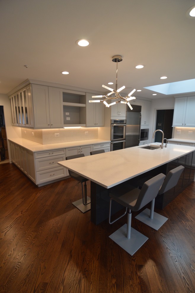 Large minimalist l-shaped medium tone wood floor and brown floor open concept kitchen photo in Chicago with an undermount sink, flat-panel cabinets, dark wood cabinets, quartz countertops, white backsplash, stone slab backsplash, stainless steel appliances and two islands