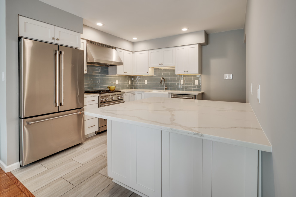 Small minimalist l-shaped vinyl floor and beige floor enclosed kitchen photo in Philadelphia with a farmhouse sink, recessed-panel cabinets, white cabinets, quartz countertops, blue backsplash, glass tile backsplash, stainless steel appliances, an island and white countertops