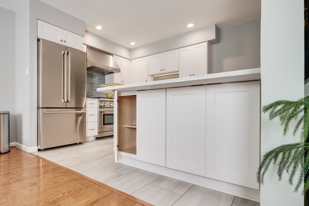 Modern inredning av ett avskilt, litet vit vitt l-kök, med en rustik diskho, luckor med infälld panel, vita skåp, bänkskiva i kvarts, blått stänkskydd, stänkskydd i glaskakel, rostfria vitvaror, vinylgolv, en köksö och beiget golv