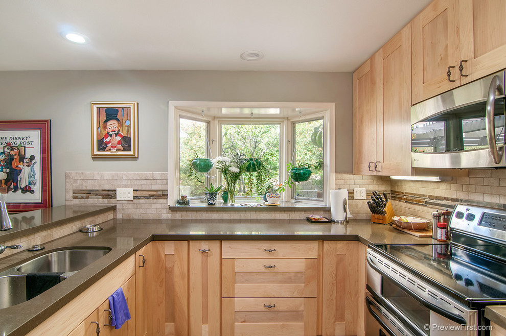 Large modern l-shaped open plan kitchen in San Diego with a double-bowl sink, shaker cabinets, light wood cabinets, engineered stone countertops, beige splashback, stone tiled splashback, stainless steel appliances, slate flooring and a breakfast bar.