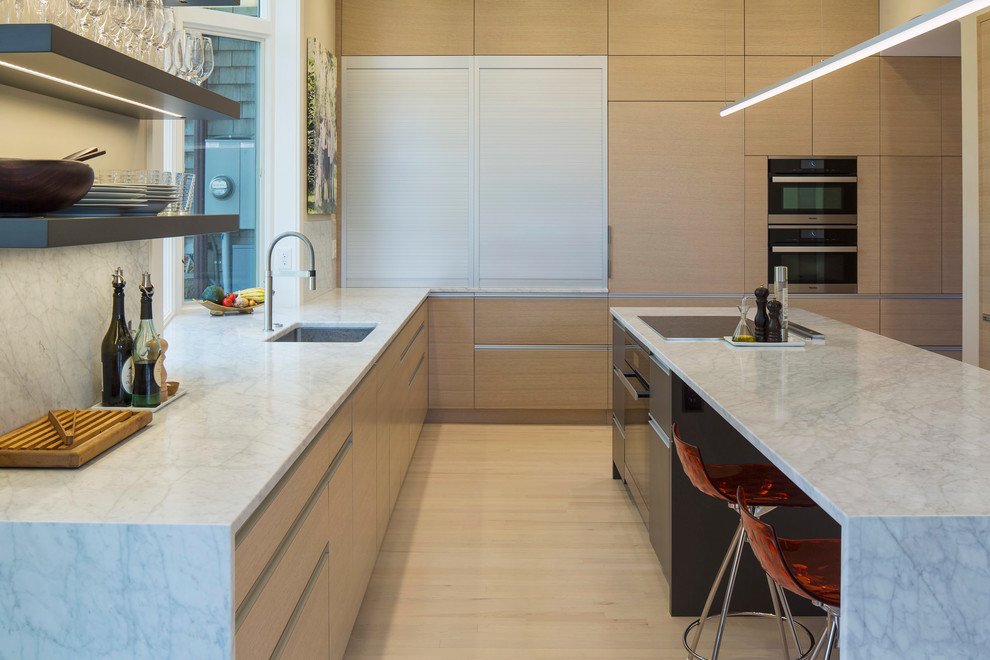 This is an example of a medium sized modern u-shaped kitchen/diner in Minneapolis with a submerged sink, flat-panel cabinets, light wood cabinets, marble worktops, white splashback, integrated appliances, light hardwood flooring and an island.
