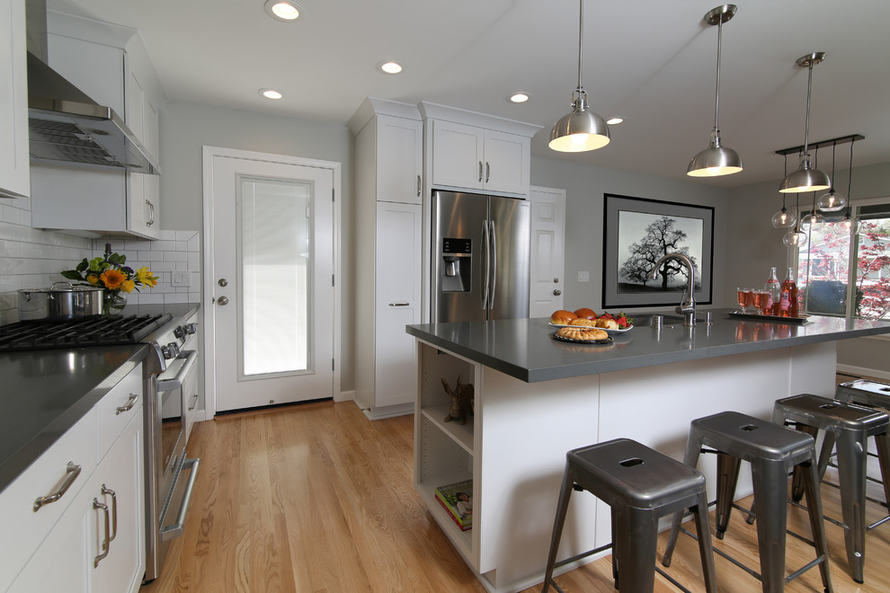This is an example of a medium sized rural single-wall kitchen/diner in San Francisco with a submerged sink, white cabinets, engineered stone countertops, white splashback, metro tiled splashback, stainless steel appliances, light hardwood flooring, an island, brown floors, shaker cabinets and grey worktops.