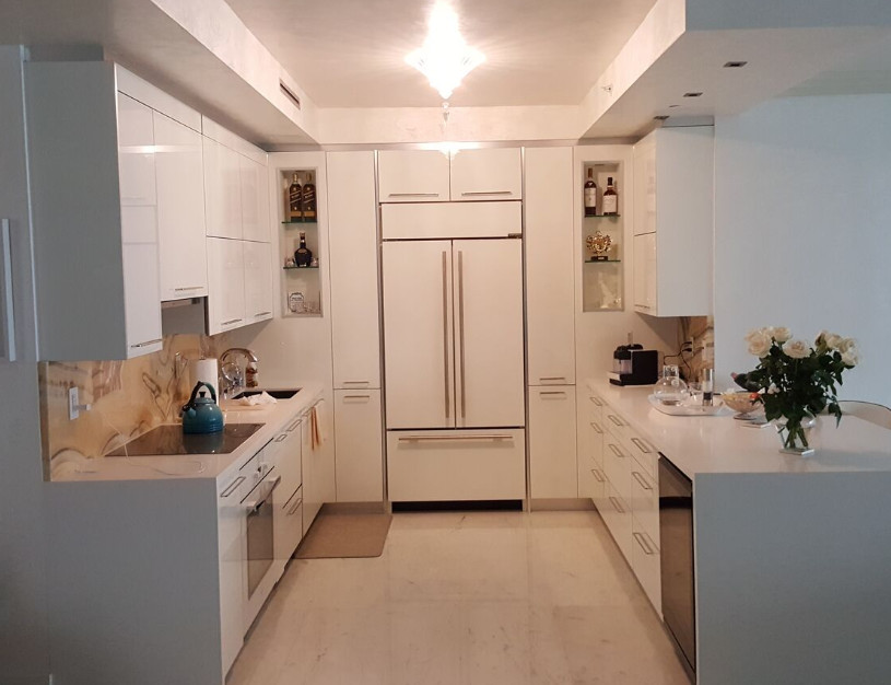 Inspiration for a small contemporary u-shaped enclosed kitchen in Miami with a submerged sink, flat-panel cabinets, white cabinets, composite countertops, beige splashback, stone slab splashback, integrated appliances, marble flooring, a breakfast bar, beige floors and white worktops.