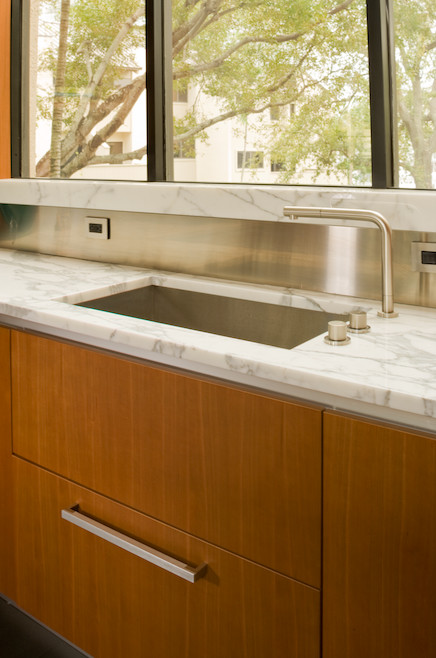 Example of a mid-sized minimalist u-shaped limestone floor enclosed kitchen design in Miami with an undermount sink, flat-panel cabinets, medium tone wood cabinets, marble countertops, metallic backsplash, stainless steel appliances and an island