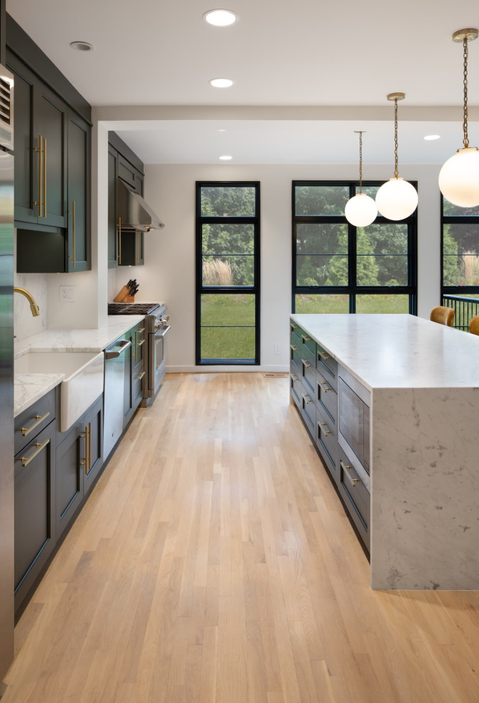 Example of a minimalist galley light wood floor and brown floor enclosed kitchen design in DC Metro with a farmhouse sink, recessed-panel cabinets, green cabinets, quartz countertops, white backsplash, stone slab backsplash, stainless steel appliances, an island and white countertops