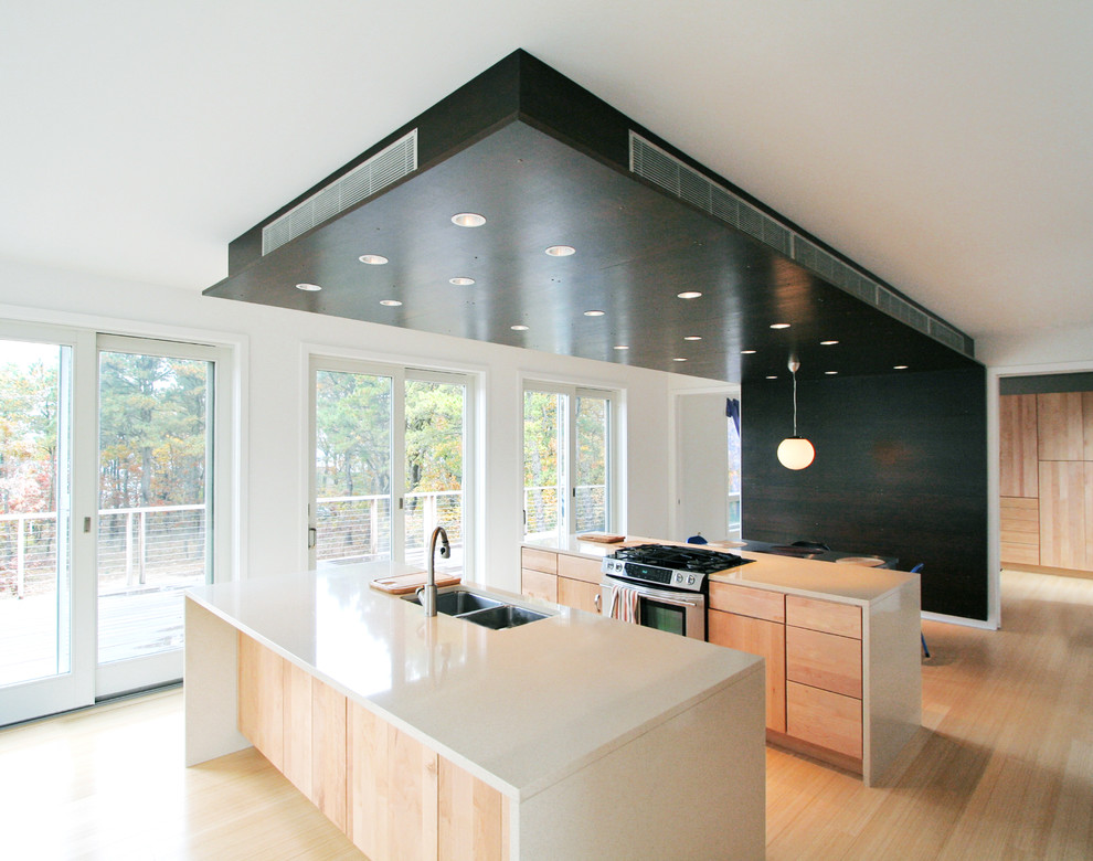 Cette photo montre une cuisine moderne en bois clair avec un électroménager en acier inoxydable, un évier 2 bacs, un placard à porte plane et un plan de travail en quartz modifié.