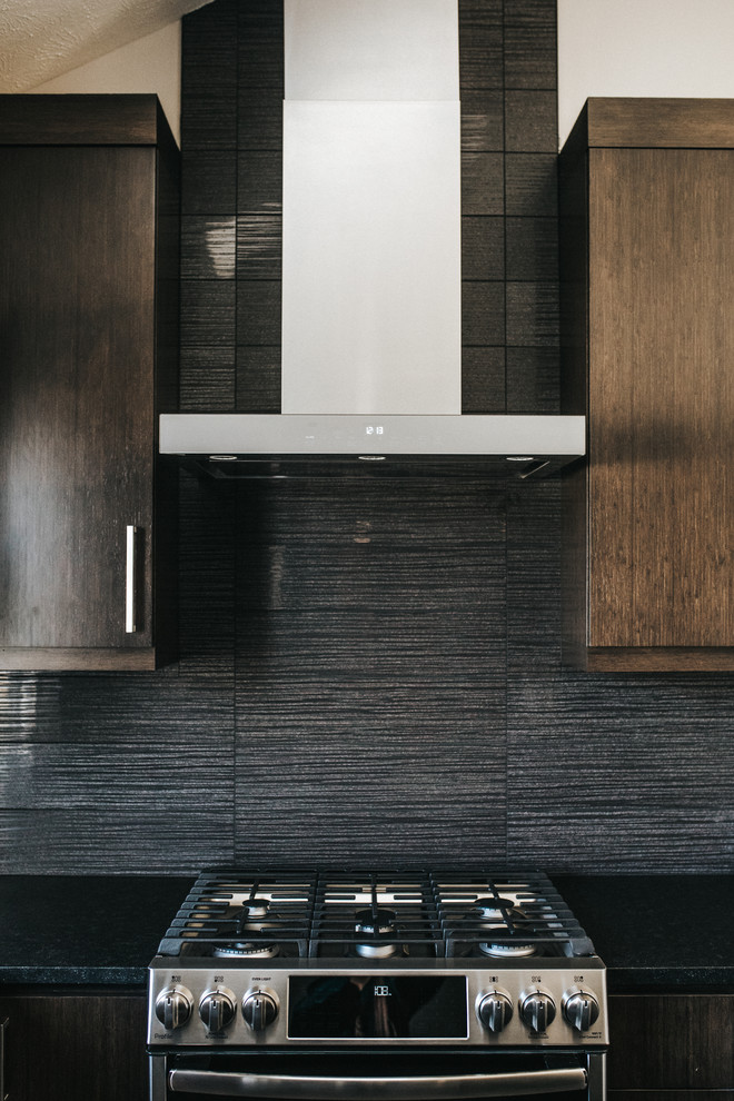 Ejemplo de cocina comedor minimalista con puertas de armario de madera en tonos medios, electrodomésticos de acero inoxidable, una isla y encimeras negras