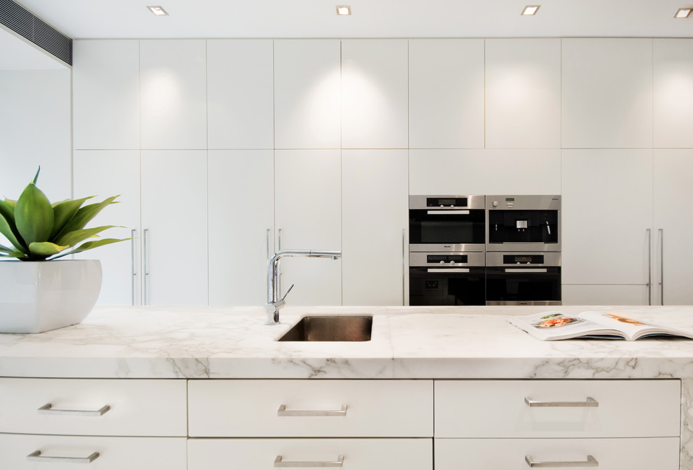Example of a large minimalist galley marble floor eat-in kitchen design in Sydney with an undermount sink, flat-panel cabinets, white cabinets, marble countertops, white backsplash, stainless steel appliances, an island and glass sheet backsplash